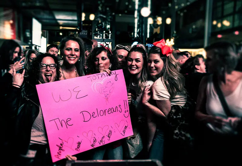 Group of girls holding a pink sign that says "we love the deloreans"
